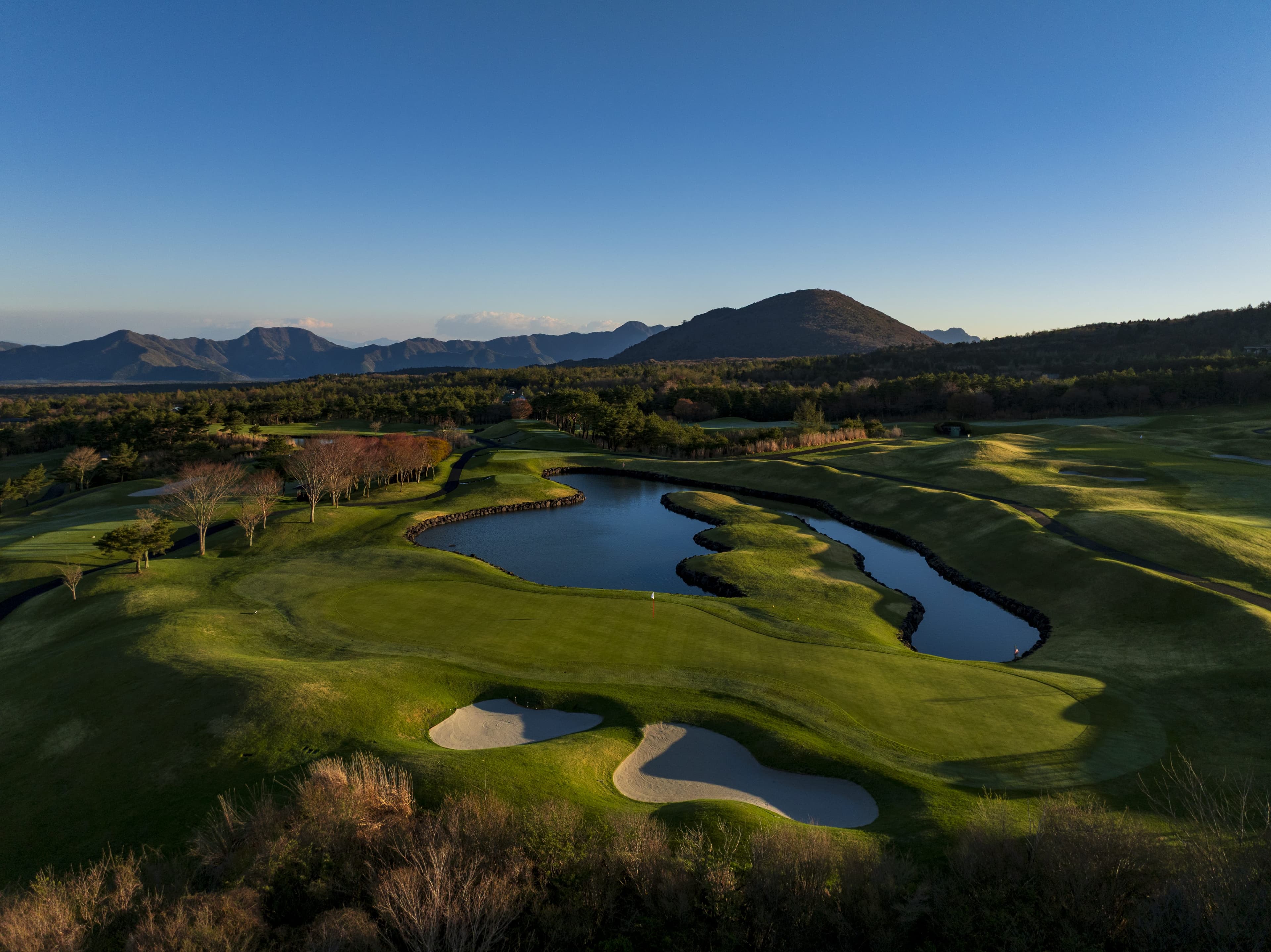 Dusk aerial of a pond-lined green with mountain ridges on the horizon