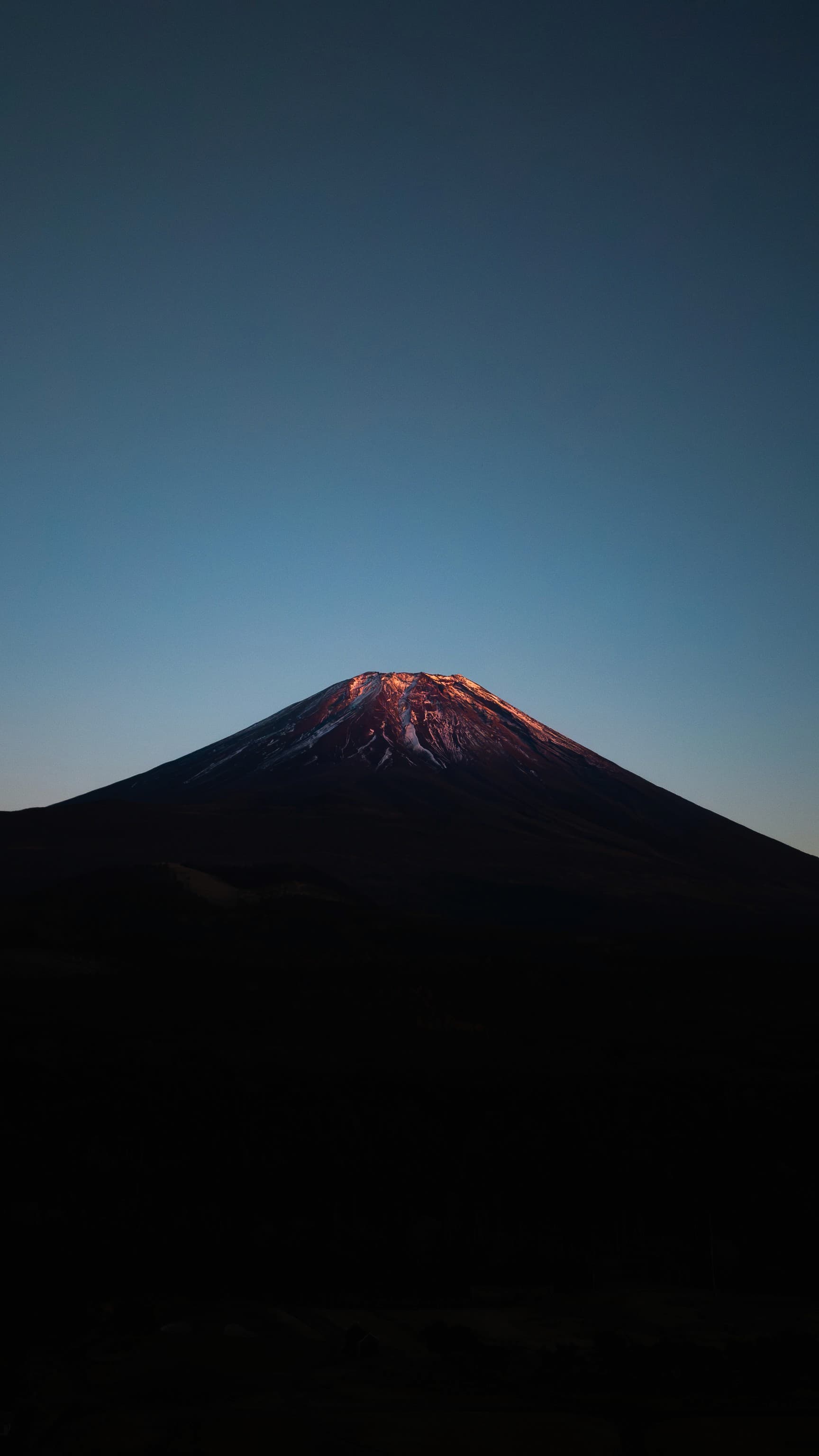 Mt. Fuji at dusk, its summit lit by the last sun