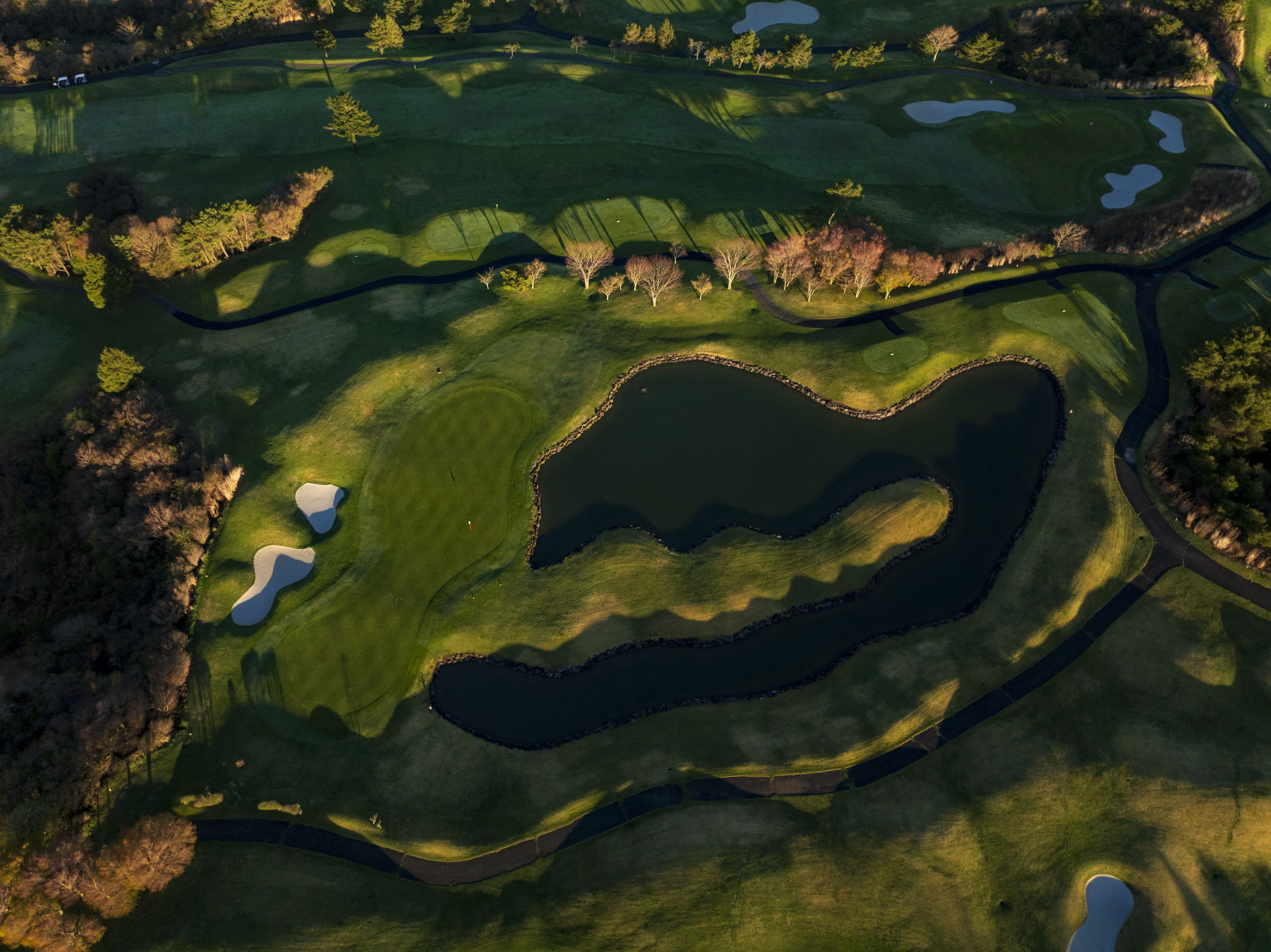 Aerial of greens and dark ponds in late-afternoon shadow
