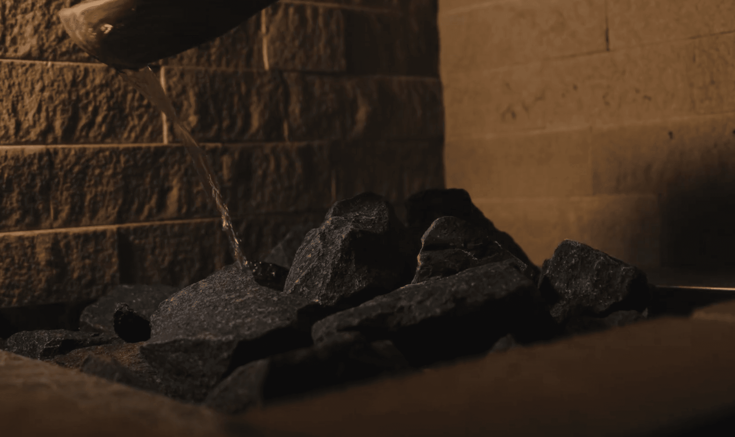 Water trickling over dark sauna stones in warm amber light