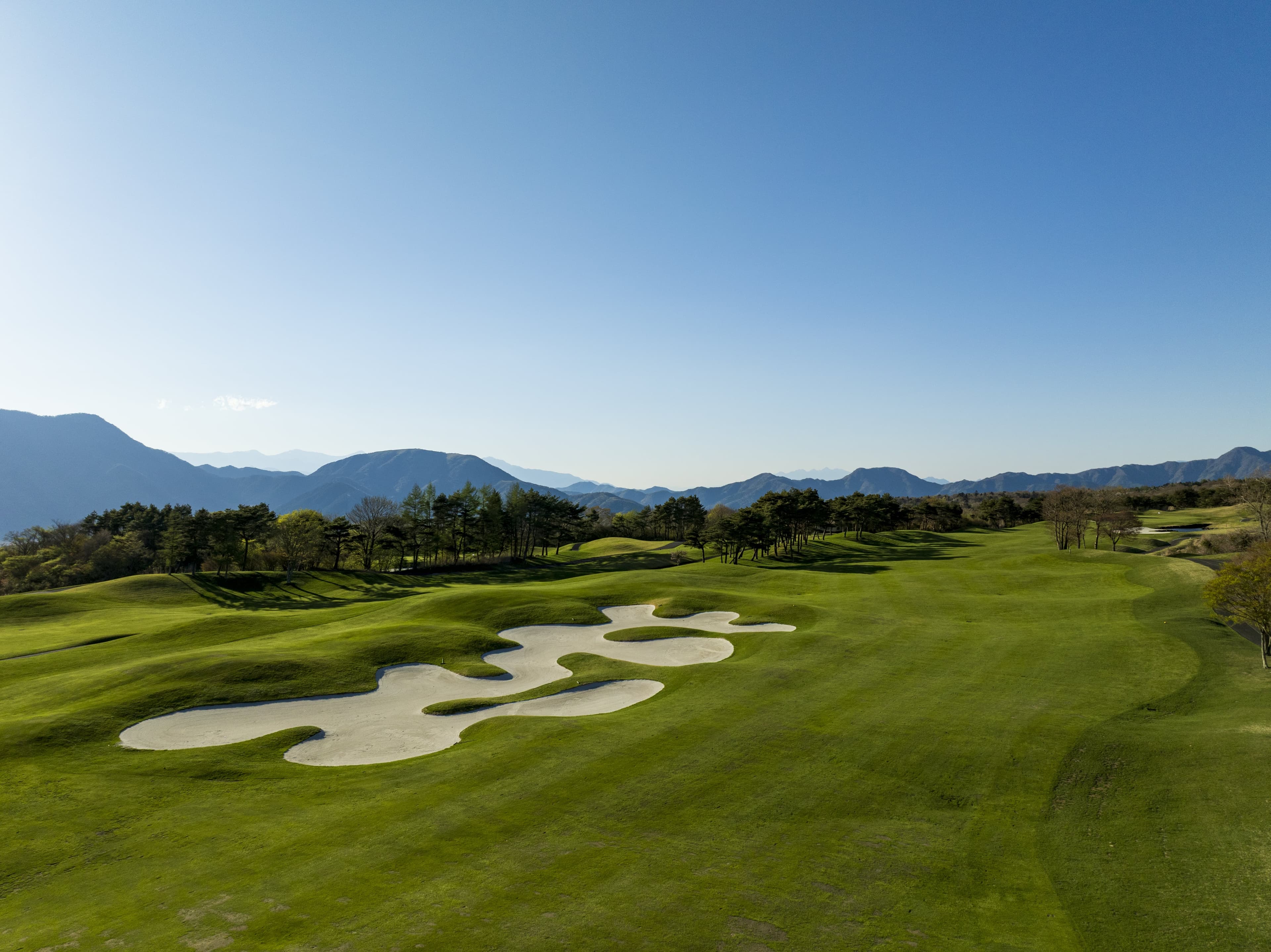 Wide fairway with white sand bunkers under a clear blue sky and distant mountains