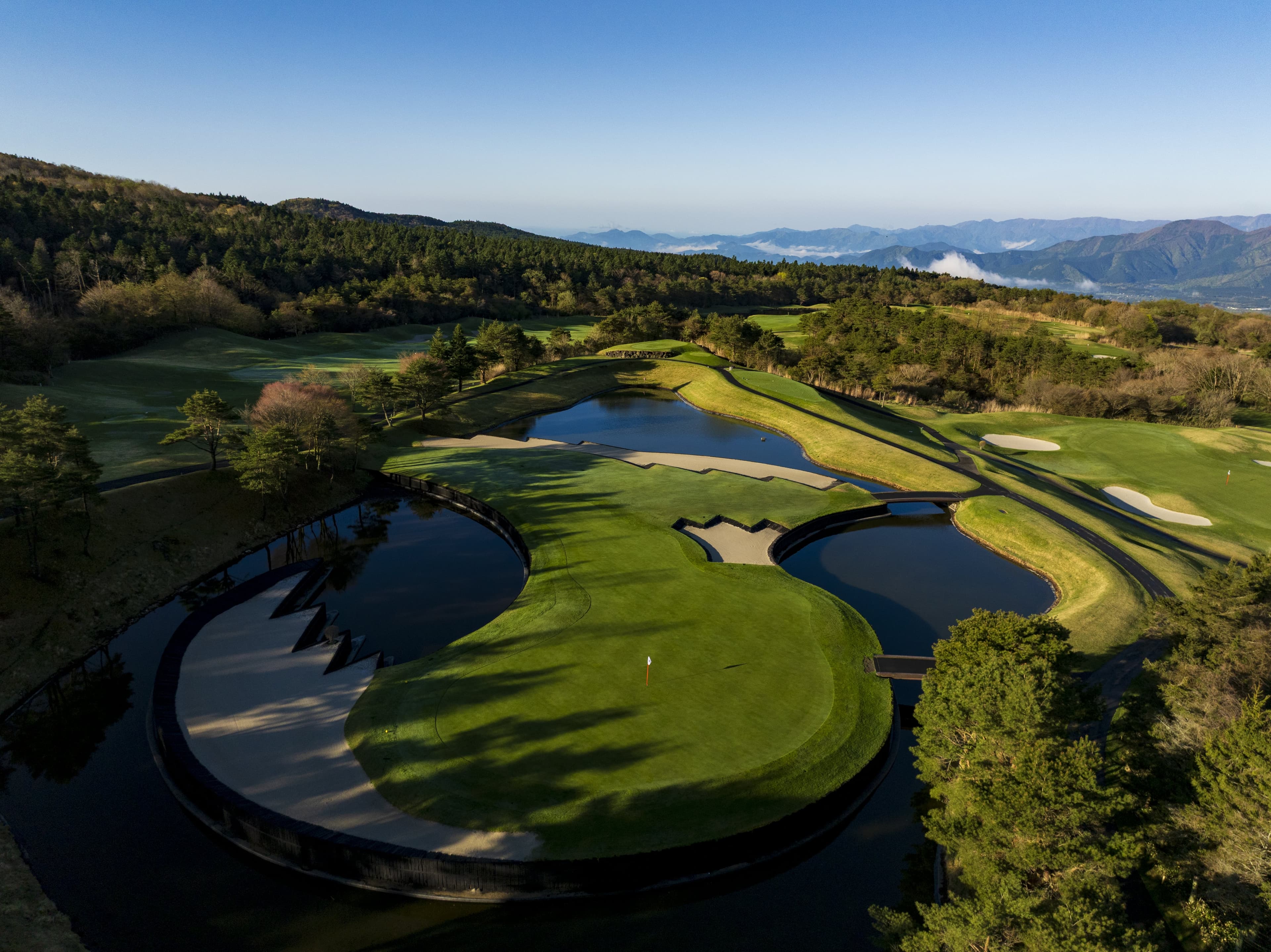 Circular water-ringed green carved into the forested hillside