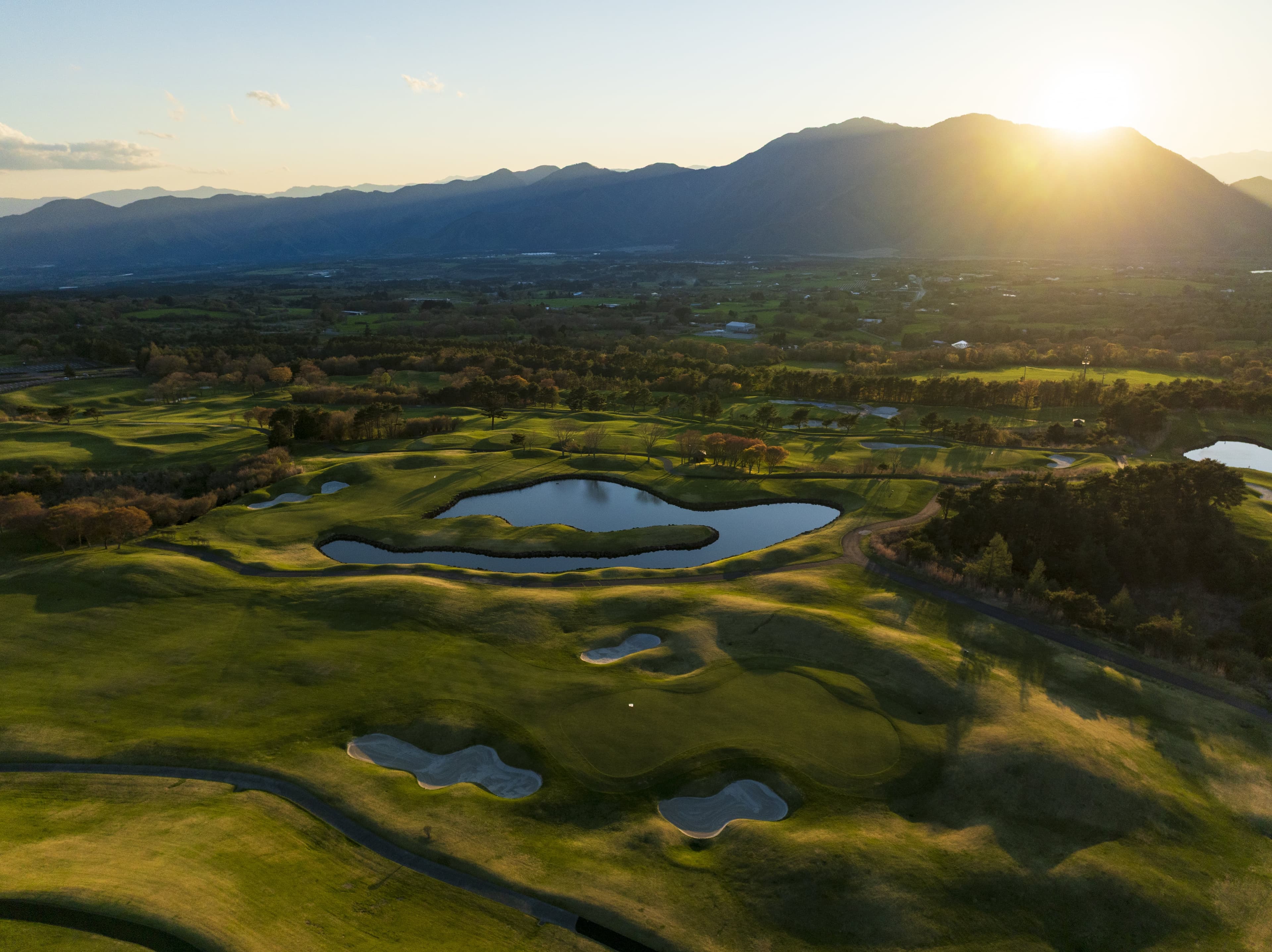 Golden-hour aerial of mounded fairways above a mountain valley