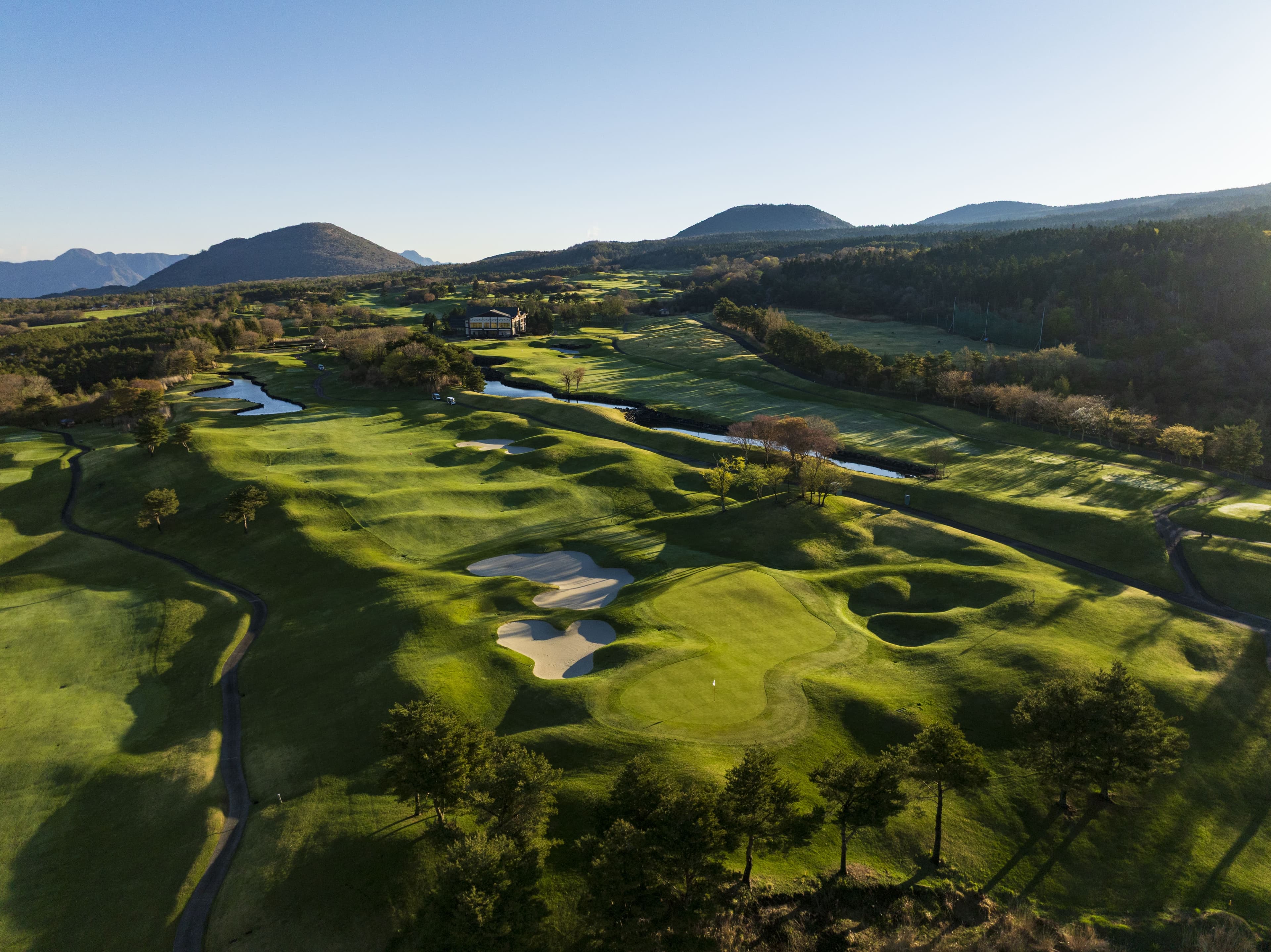 Aerial view of rolling fairways and sand bunkers winding between pine forest and ponds