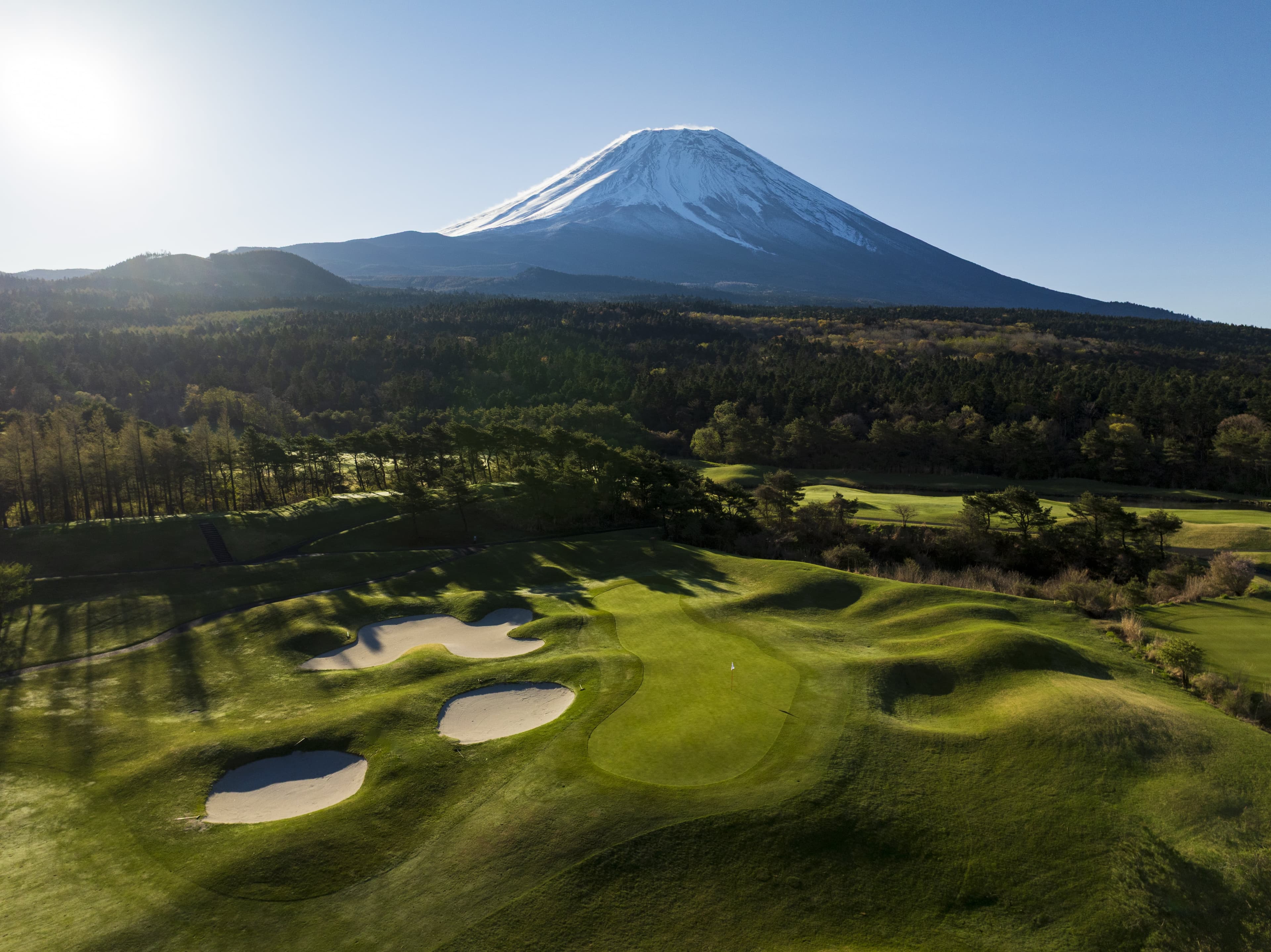 Snow-capped Mount Fuji towering over bunkered fairways in morning light
