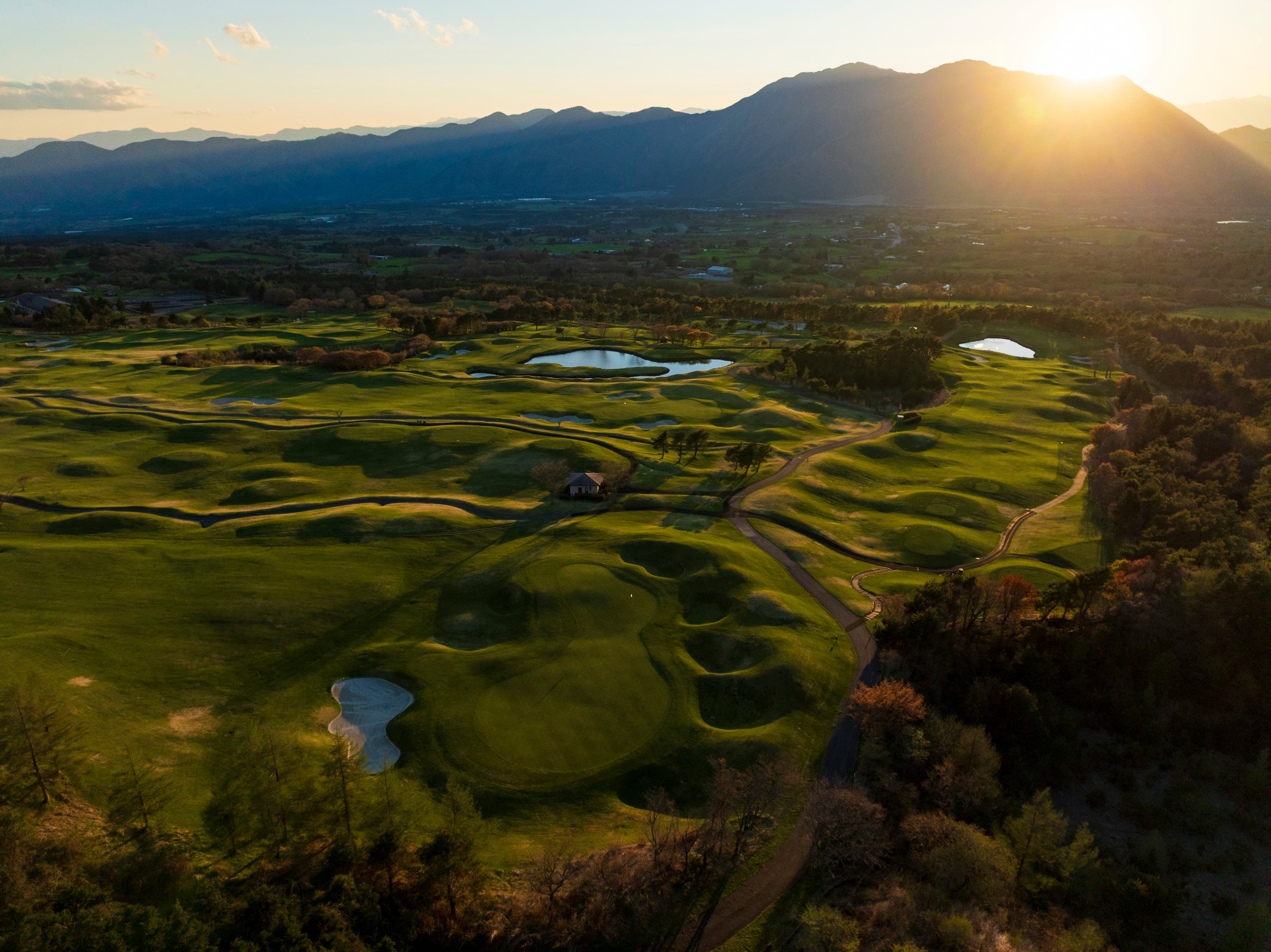 Aerial view of the Fuji Classic course at sunset, mountains glowing on the horizon